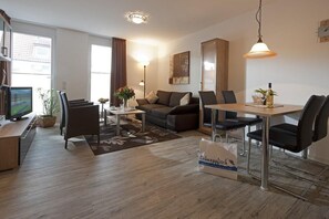 A modern living room with a sofa, coffee table, and dining area. There is a television, a plant, and a bag on the floor. - Exklusive Ferienwohnung für Gehobene Ansprüche auf Norderney (Norderney)