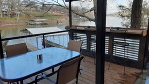 A covered outdoor deck with a table and chairs, overlooking a lake with docks and boats.