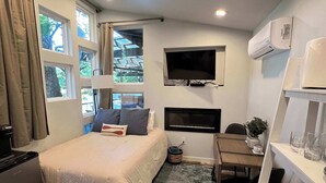 A compact hotel room with a bed, a desk, a TV, and an air conditioning unit.