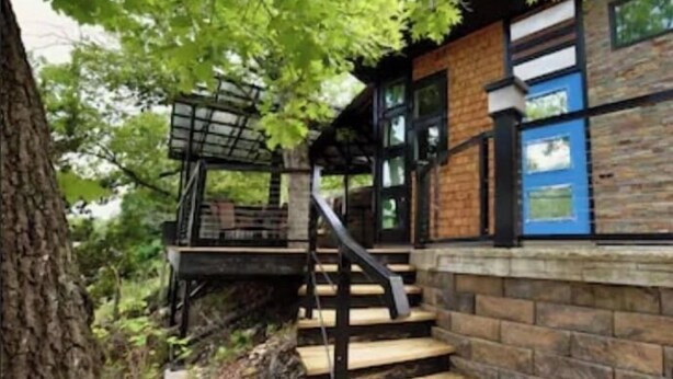 A staircase leading to a wooden deck with a metal railing, surrounded by trees.