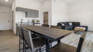 Een moderne keuken met grijze kastjes, een eethoek met een houten tafel en stoelen, en een grijze bank in een woonkamer.