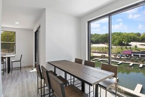 Un espace de restauration moderne, doté d’une grande table et de chaises, de larges fenêtres offrant une vue sur un élément aquatique et de la verdure.