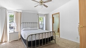 A bedroom with a bed, a ceiling fan, a window with curtains, and a door.
