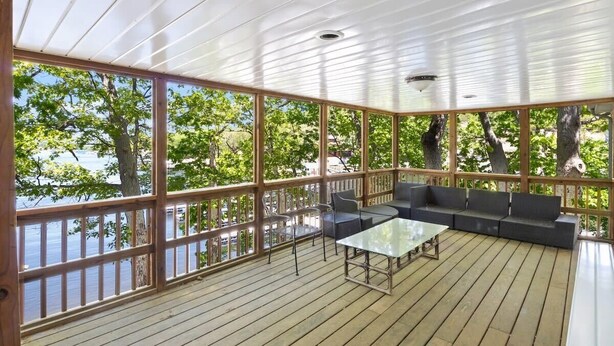A covered outdoor area with a wooden deck, a glass table, and a sofa.
