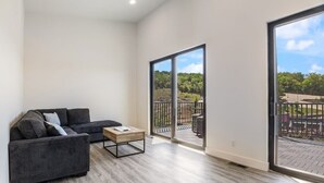 A spacious living room with a grey sofa, a wooden coffee table, and a large sliding glass door leading to an outdoor balcony.