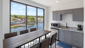 A modern kitchen with a large window, a dining area with a table and chairs, and a view of a marina.