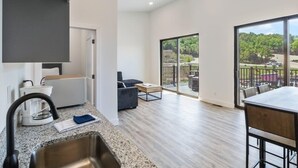 A modern kitchen with a large window, a dining area with a table and chairs, and a balcony with outdoor seating.