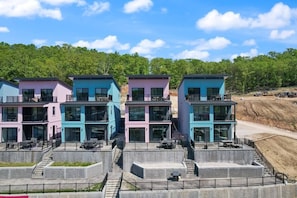 A row of modern, multi-story buildings with balconies, situated on a concrete platform with a view of a forested hillside. - 1177 New Lakefront 5 bd. Sleeps 16 Backwater Jacks (Lake Ozark)