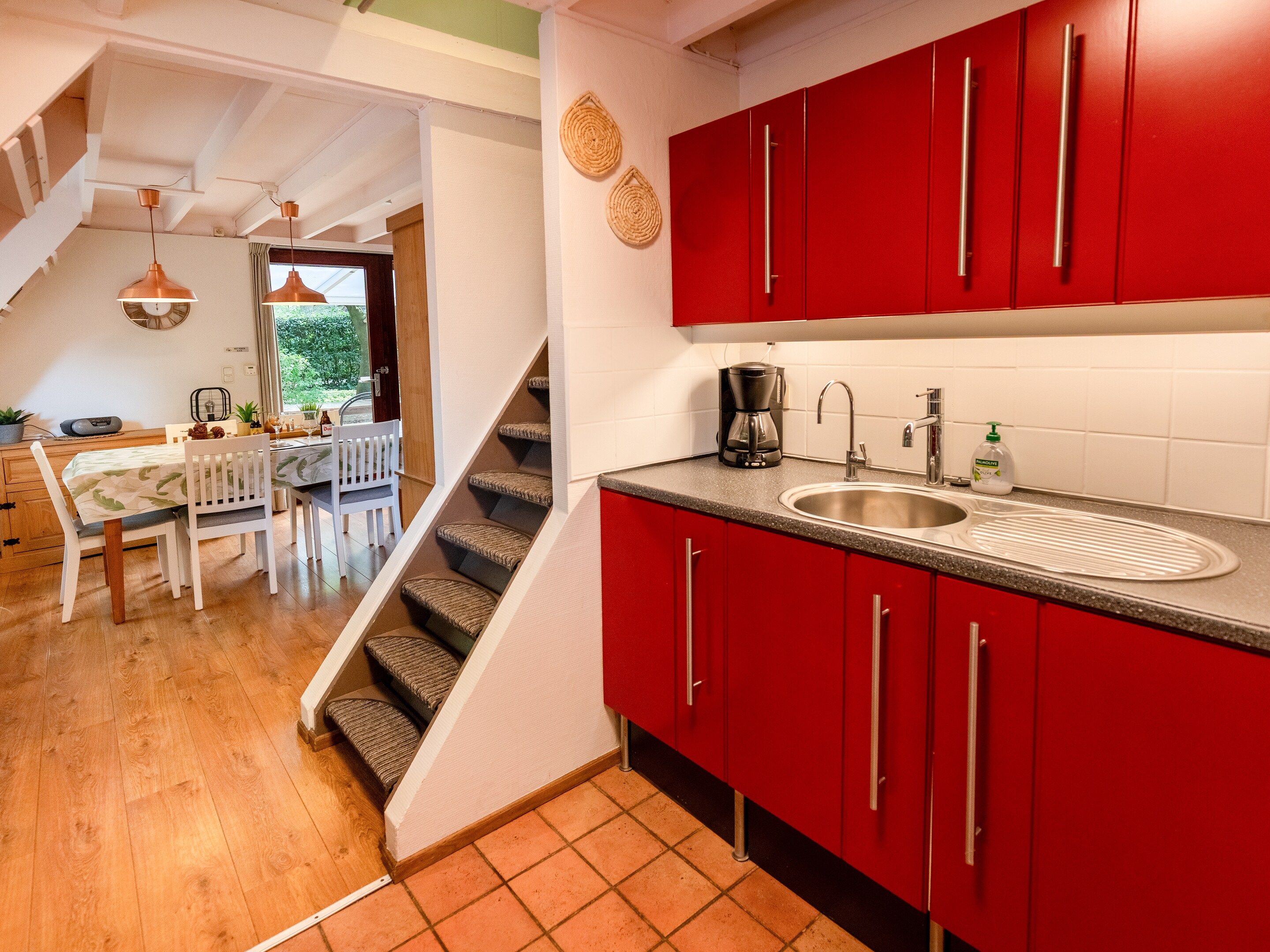 A kitchen with red cabinets, a sink, and a coffee maker.