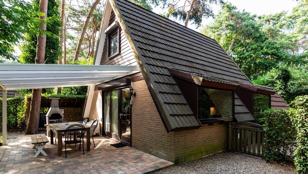 A cozy cabin with a sloped roof, a patio with a table and chairs, and a brick exterior. - Cozy Garden Retreat in Lanaken (Lanaken)