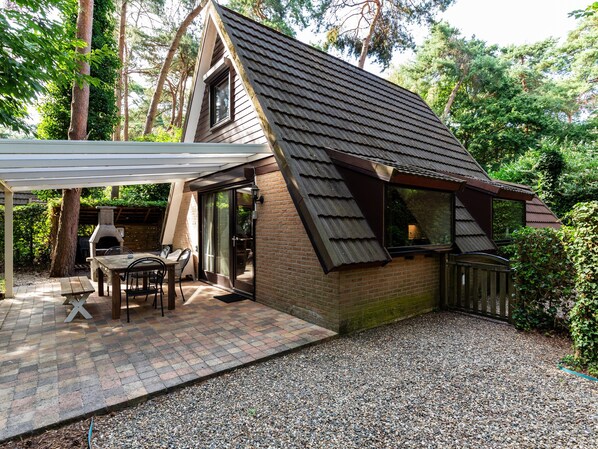 A cozy cabin with a sloped roof, a patio with a table and chairs, and a brick exterior. - Cozy Garden Retreat in Lanaken (Lanaken)