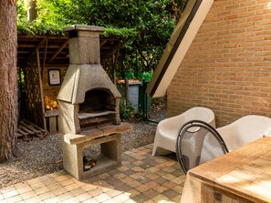 An outdoor stone pizza oven with a brick wall and a wooden table nearby. - Cozy Chalet With Sauna in Lanaken (Lanaken)