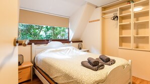 A bedroom with a bed, a bedside table, a window with a view of trees, and a built-in shelving unit. - Cozy Garden Retreat in Lanaken (Lanaken)