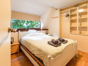 A bedroom with a bed, a bedside table, a window with a view of trees, and a built-in shelving unit. - Cozy Garden Retreat in Lanaken (Lanaken)