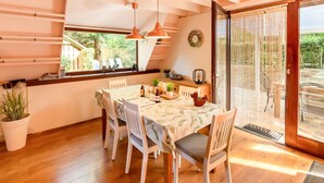 A dining area with a table set for four, wooden chairs, pendant lights, a window with a view of greenery, and a sliding glass door leading outside. - Cozy Garden Retreat in Lanaken (Lanaken)