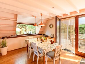 A dining area with a table set for four, wooden chairs, pendant lights, a window with a view of greenery, and a sliding glass door leading outside. - Cozy Garden Retreat in Lanaken (Lanaken)