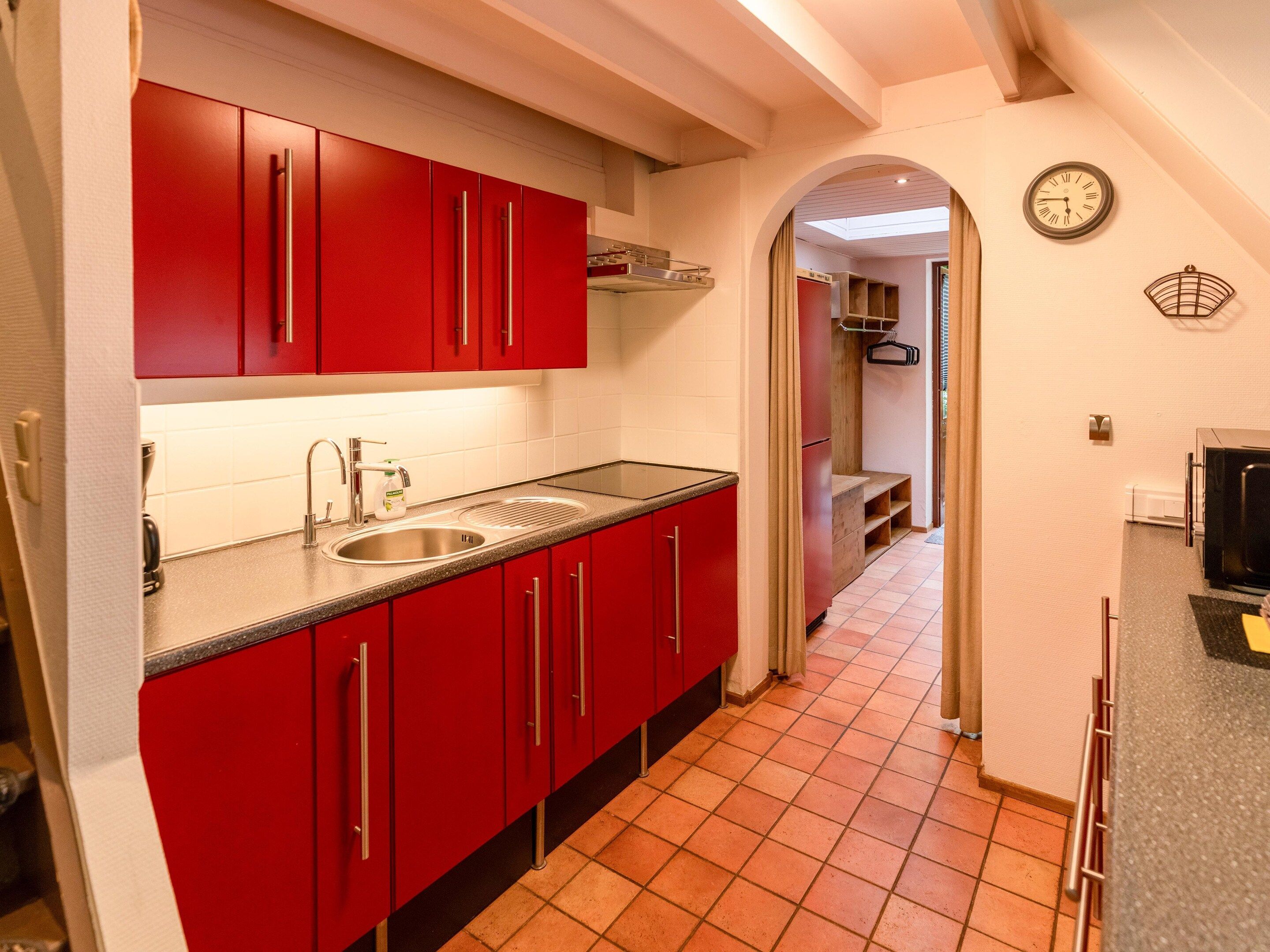 Een kleine keuken met rode kastjes, een roestvrijstalen spoelbak en een betegelde vloer.