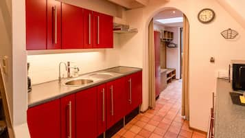A compact kitchen with red cabinets, a stainless steel sink, and a tiled floor.