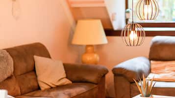 A living room with a brown sofa, a lamp, a potted plant, and a remote control on a wooden table.