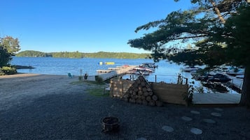 Un'area sterrata con un pontile in legno, una catasta di legna e un piccolo braciere.
