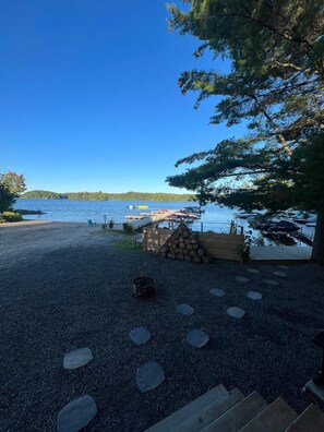 A gravel area with a wooden deck, a pile of logs, and a small fire pit. - Terrawoods Resort Muskoka  (Seguin)