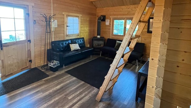A log cabin interior with a loft bed, a fireplace, a sofa, and a dining table.