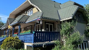 A two-story house with a steeply pitched roof, a blue front porch, and a stone pathway leading to the entrance.