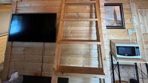 A wooden interior with a wooden staircase, a flat-screen TV, a microwave, and a framed picture on the wall.