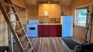 A wooden cabin interior with a kitchen area, including a stove, sink, and cabinets.