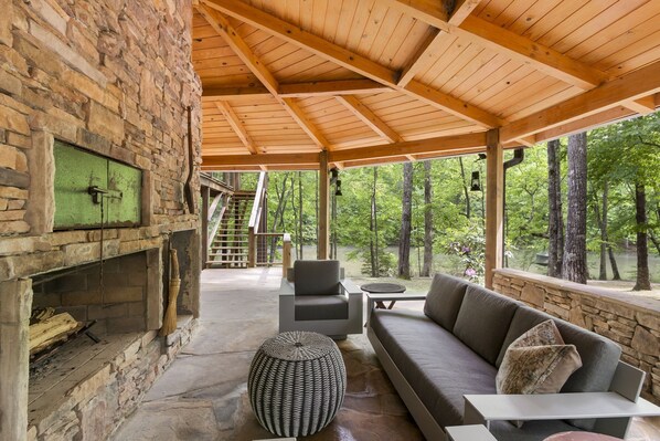 A covered outdoor seating area with a stone fireplace, a sofa, and a table.