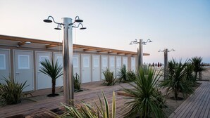Una hilera de cabañas frente a la playa, con terraza de madera y plantas en macetas.