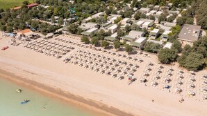 An aerial view of a beachside resort with multiple bungalow-style accommodations, a sandy beach, and umbrellas.