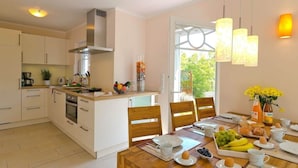 A modern kitchen with white cabinets, a central island, and a dining area with wooden chairs and a table set for breakfast. - Holiday Home Bloom 2 (Zingst)