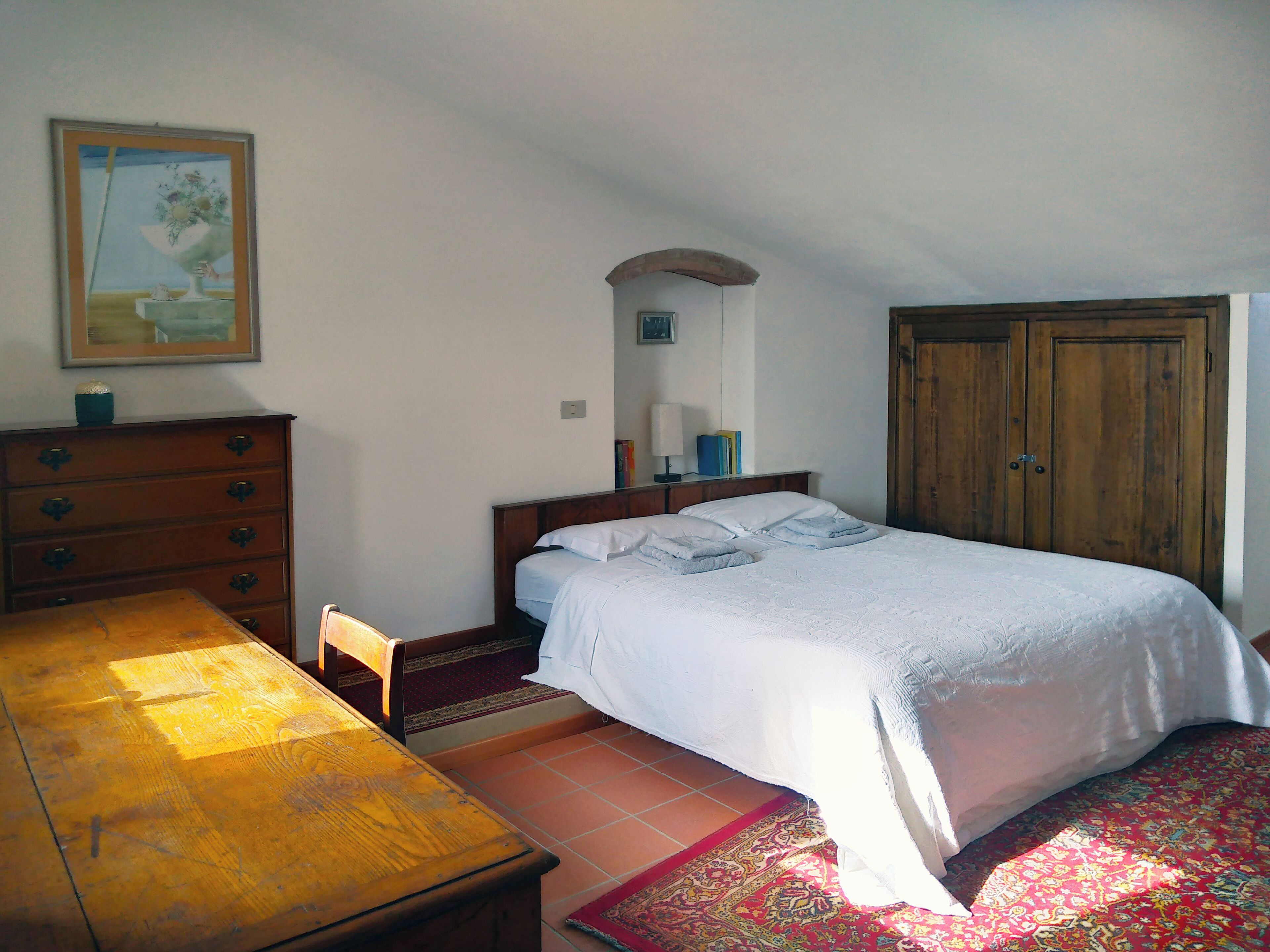 A bedroom with a bed, wooden dresser, and a painting on the wall.