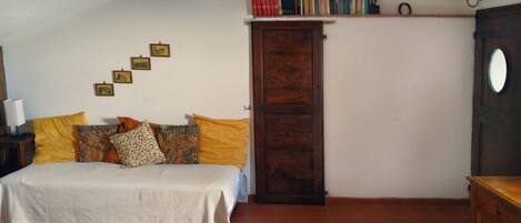 Un dormitorio con una cama, un armario de madera, una estantería con libros y una alfombra estampada.