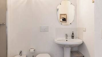 A bathroom with a bidet, toilet, sink, and a mirror.