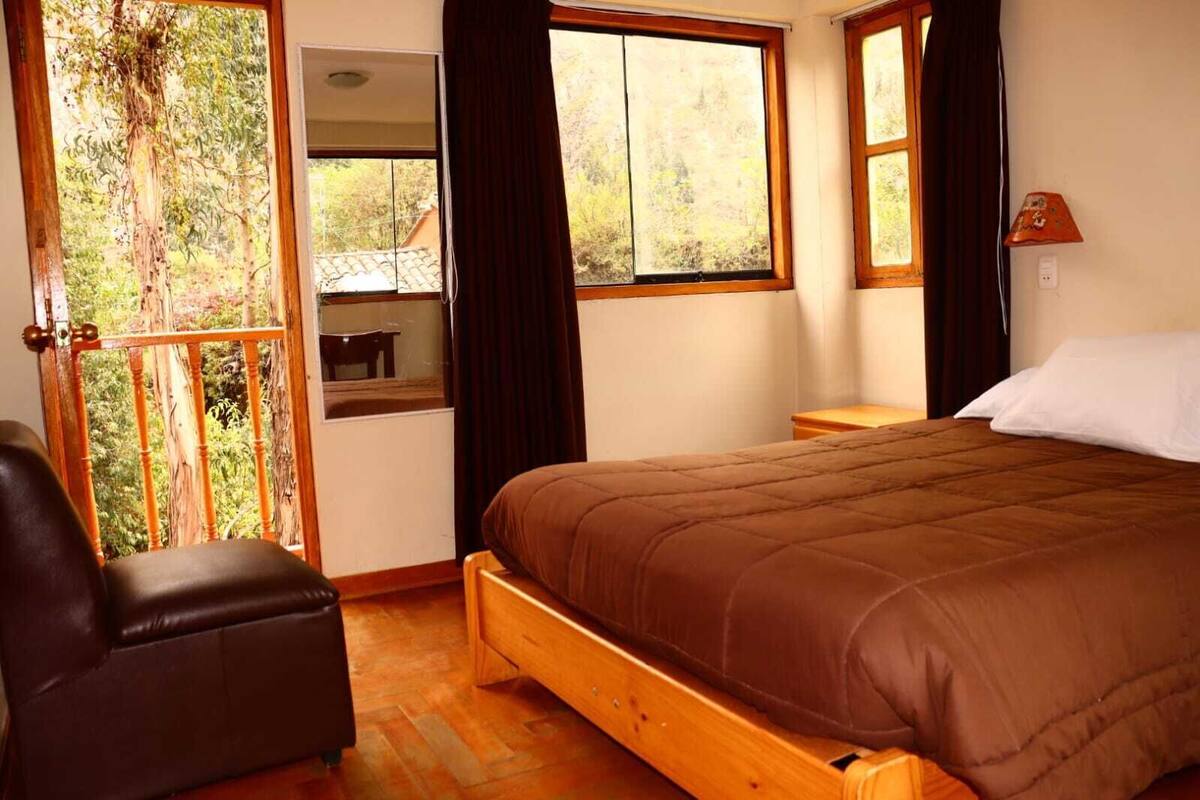 A bedroom with a wooden bed, a chair, a small table, and a window with curtains.