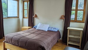 A bedroom with a wooden bed, two bedside tables, a nightstand, a small wooden shelf, and a window with curtains. - Full Moon Eco Lodge (Ollantaytambo)