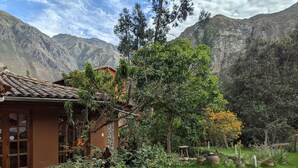 A rustic house with a tiled roof, surrounded by a lush garden and mountains in the background. - Full Moon Eco Lodge (Ollantaytambo)