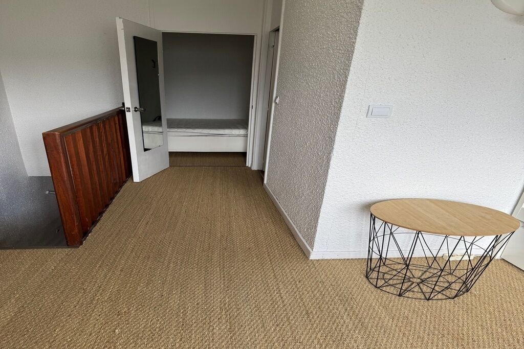 A hallway with a wooden bench, a small round table with a geometric base, and a closet with a mirrored closet rod.