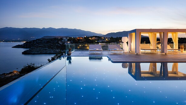 Une piscine à débordement moderne offrant une vue dégagée sur la mer et les montagnes en arrière-plan.