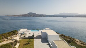 Une villa moderne dotée d’une piscine sur le toit, offrant une vue imprenable sur une mer calme et des montagnes lointaines.