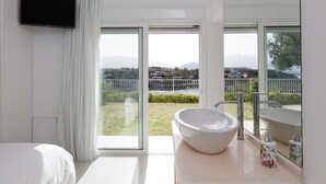 Une salle de bain moderne avec une grande fenêtre, un lavabo blanc et un téléviseur à écran plat fixé au mur.