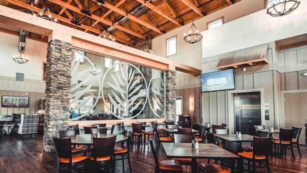A restaurant with wooden beams, stone pillars, and a large decorative wall. Tables and chairs are arranged for dining. - Cincinnati Camp Cedar (Mason)