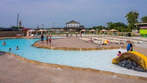 A pool area with multiple swimming pools, lounge chairs, and a building in the background. - Cincinnati Camp Cedar (Mason)