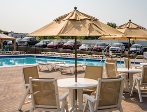 A poolside area with lounge chairs and umbrellas, a swimming pool, and a parking lot with cars. - Cincinnati Camp Cedar (Mason)