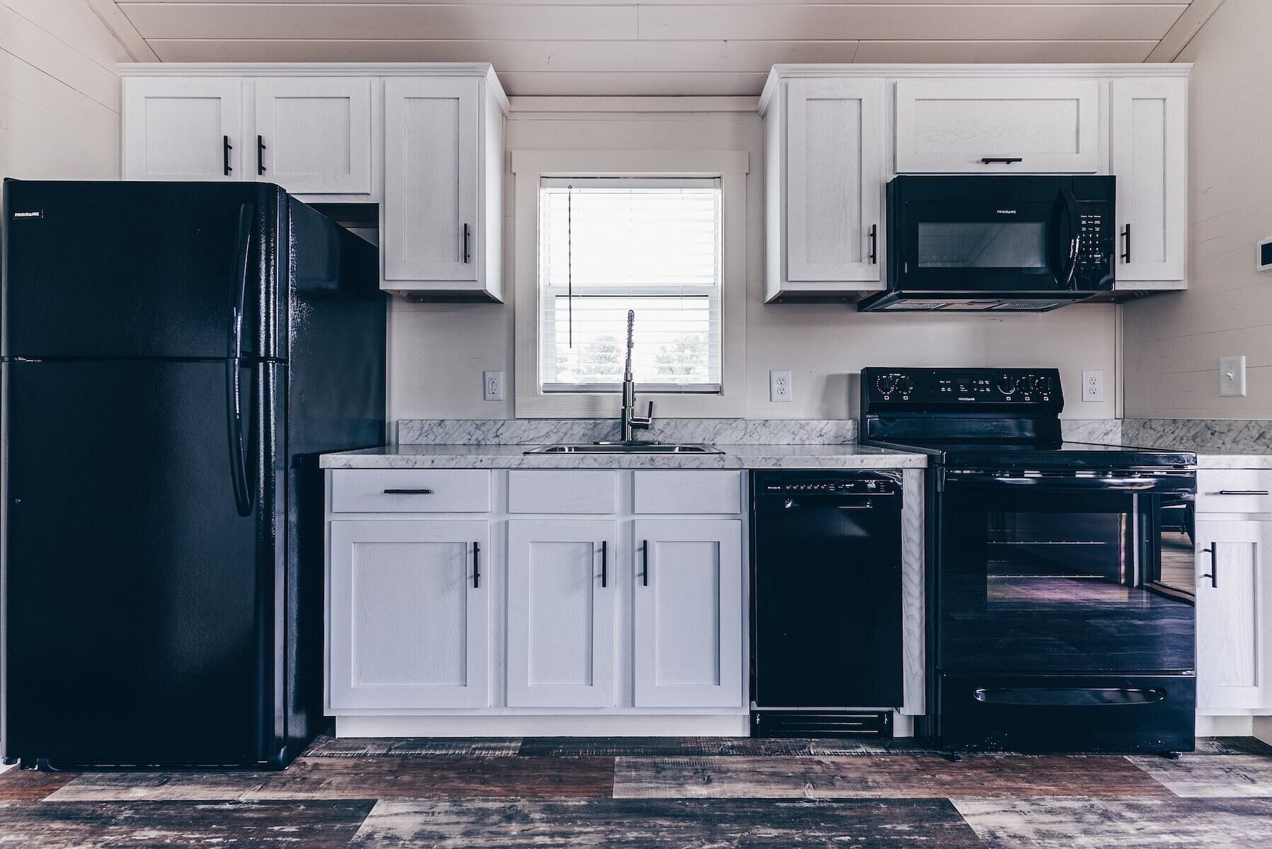 Una cocina con armarios blancos, un refrigerador negro, un microondas, un lavavajillas y un horno.