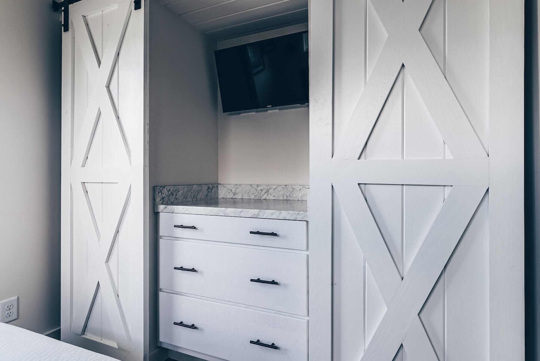 A bathroom with a white vanity, a mirror, and a TV mounted above the mirror.