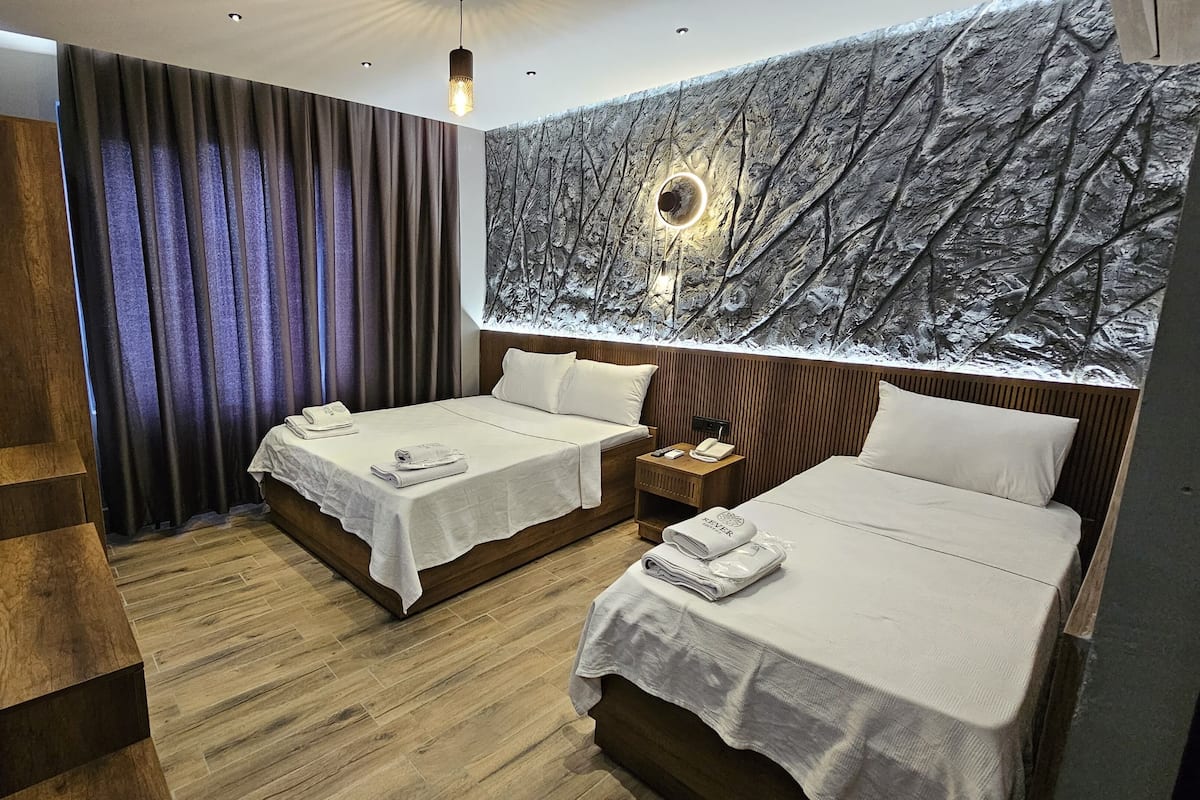 Une chambre d’hôtel avec deux lits, un plancher en bois, une grande fresque murale, une télévision et une table de chevet en bois.