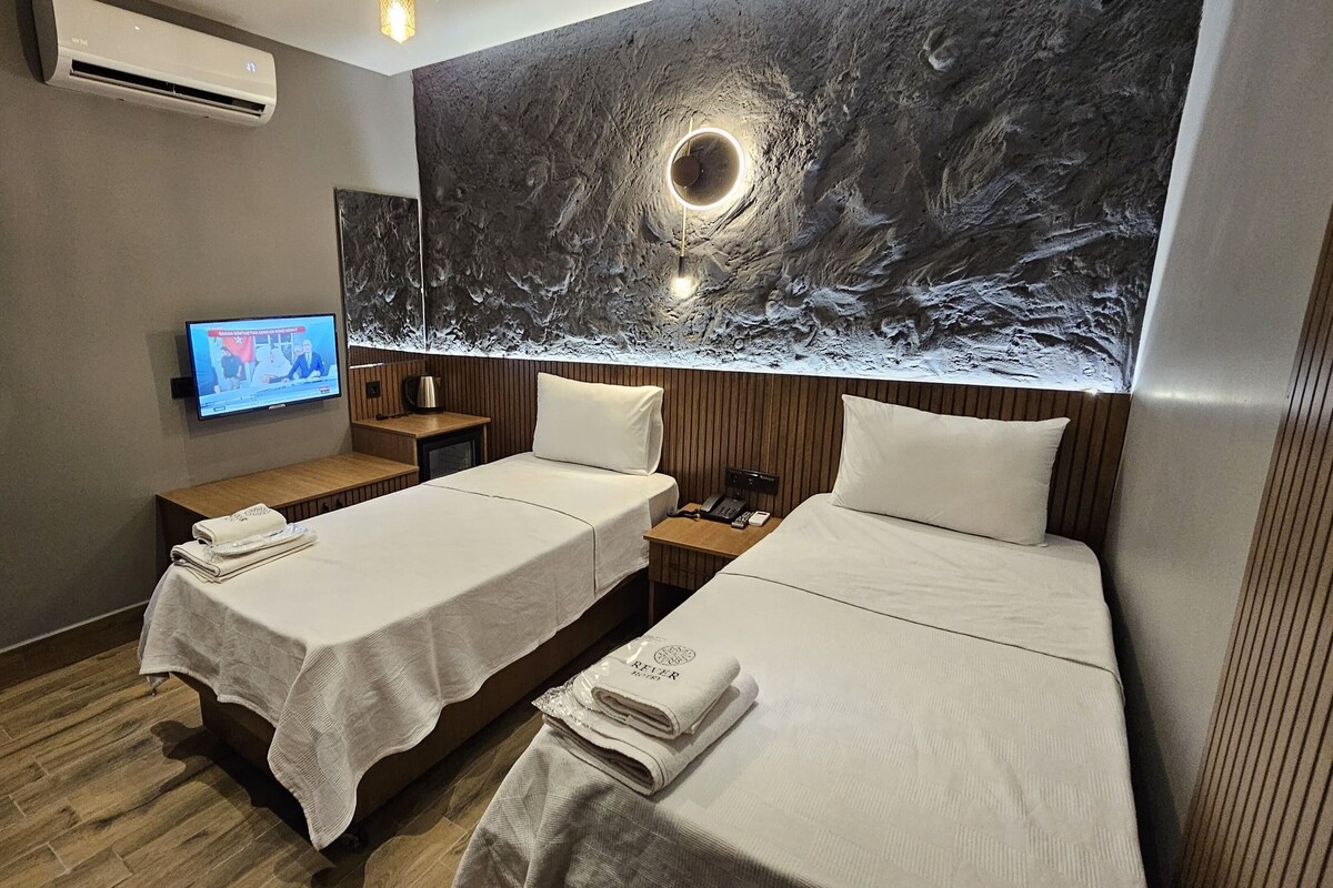 Habitación de hotel con dos camas, televisión, aire acondicionado de pared y un cuadro abstracto grande.